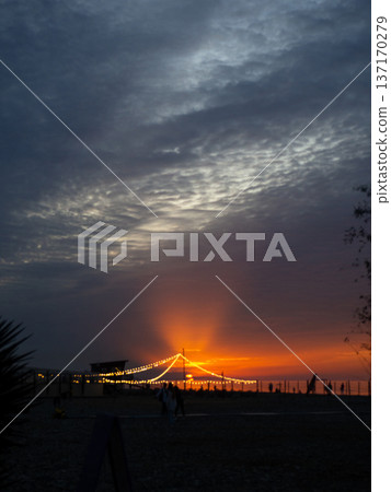 Bright sunset against the backdrop of a restaurant on the seashore. Restaurant lights. Sunset at the resort. 137170279