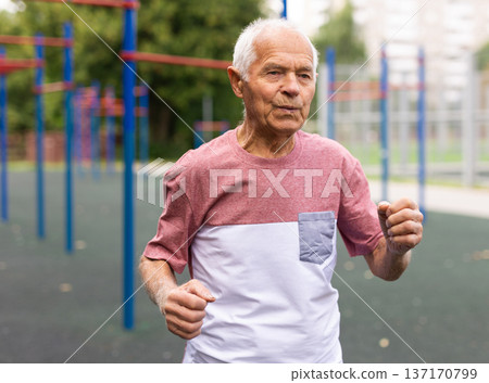 Old man running beside playground in urban park 137170799