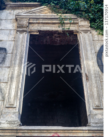 An abandoned building from the last century. Window overgrown with plants. Destroyed building. Emptiness and melancholy. Nature and city. 137170914