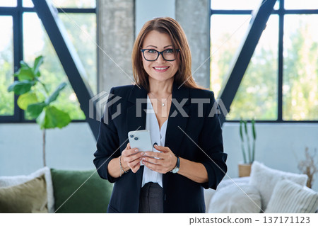 Portrait of smiling middle-aged businesswoman with smartphone in office with couch 137171123