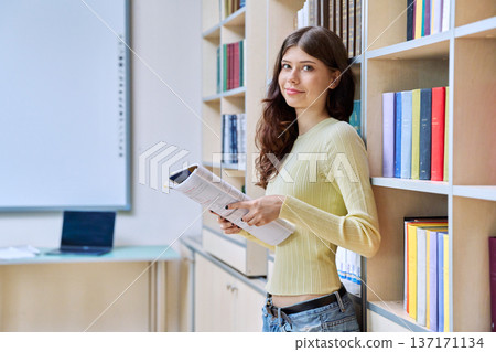 Portrait of teenage beautiful girl high school student with textbook in library classroom Portrait of teenage beautiful girl high school student with textbook in library classroom 137171134