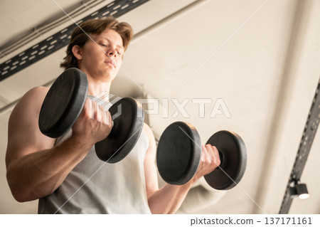 Young man doing dumbbell biceps curl in fitness club Young man doing dumbbell biceps curl in fitness club 137171161