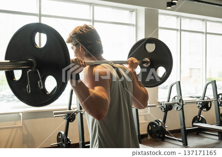 Young man doing barbell back squat in modern gym Young man doing barbell back squat in modern gym 137171165