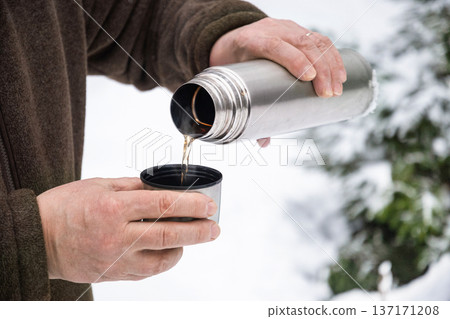 Pouring hot drink from thermos into metal cup in winter outdoors Pouring hot drink from thermos into metal cup in winter outdoors 137171208