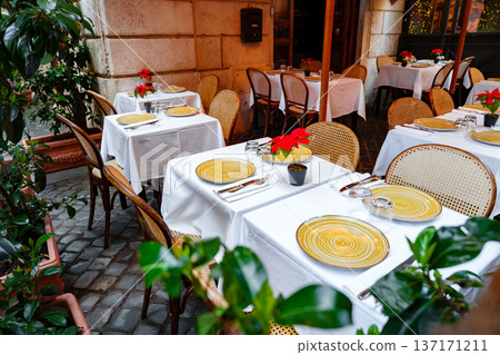 Outdoor dining area at a cafe with tables and chairs in a lively setting during the daytime Outdoor dining area at a cafe with tables and chairs in a lively setting during the daytime 137171211