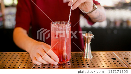 Stirring drink. Cocktail recipe. Bartender mixing flavored refreshing beverage with long metal spoon. Professional metal jigger for measuring. 137171503