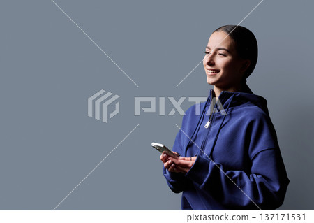 Portrait of smiling teenage girl holding smartphone on gray studio background Portrait of smiling teenage girl holding smartphone on gray studio background 137171531