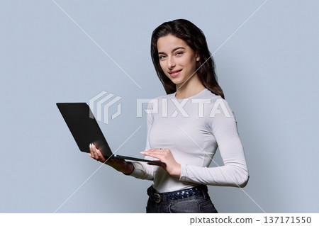 Portrait of smiling teenage girl using laptop on gray background Portrait of smiling teenage girl using laptop on gray background 137171550