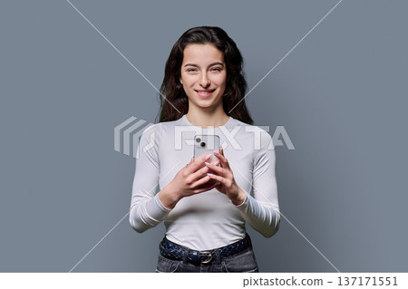 Portrait of smiling teenage girl holding smartphone on gray studio background Portrait of smiling teenage girl holding smartphone on gray studio background 137171551