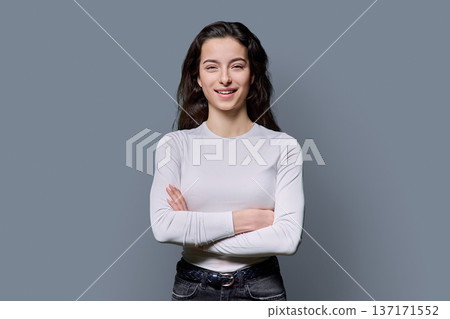 Beautiful young woman with crossed arms looking at camera on grey background Beautiful young woman with crossed arms looking at camera on grey background 137171552