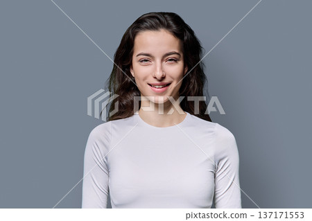 Portrait of beautiful smiling teenage woman against grey studio background Portrait of beautiful smiling teenage woman against grey studio background 137171553