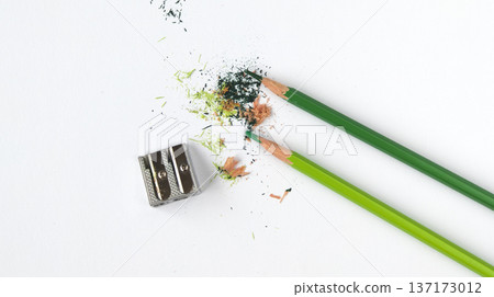 Two green colored pencils with a metal sharpener, wood shavings, and colored pigment. Education, hobby, and art concept. Two green colored pencils with a metal sharpener, wood shavings, and colored pigment. Education, hobby, and art concept. 137173012