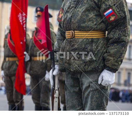 Military field uniform Russian soldier during parade rehearsal, with colors of national flag in background. Military field uniform Russian soldier during parade rehearsal, with colors of national flag in background. 137173110