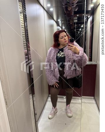 Woman taking a selfie in an elevator wearing a lilac faux fur coat. Confidence, style, and individuality expressed through playful urban fashion. Woman taking a selfie in an elevator wearing a lilac faux fur coat. Confidence, style, and individuality expressed through playful urban fashion. 137173450