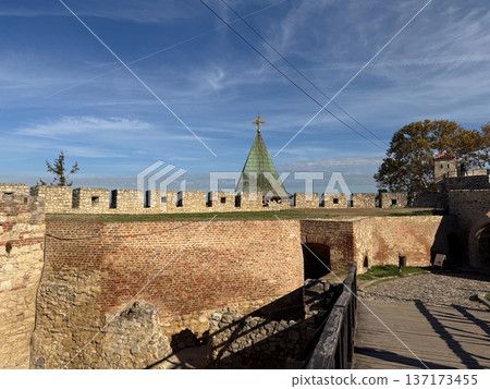 Historic fortress tower behind brick wall under blue sky in Belgrade. Heritage, architecture and cultural preservation in urban environment. Historic fortress tower behind brick wall under blue sky in Belgrade. Heritage, architecture and cultural preservation in urban environment. 137173455