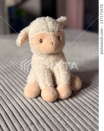 Plush toy lamb on gray corduroy sofa in soft daylight close-up. Cozy home interior, childhood nostalgia and gentle warmth captured through texture and simplicity 137173478