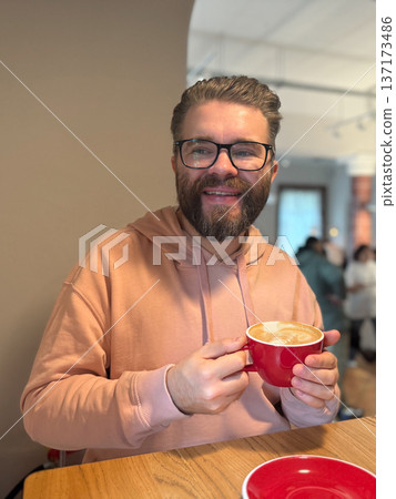 Man smiling with cup of coffee in modern cafe. Expression of joy, warmth and everyday connection over morning beverage. 137173486
