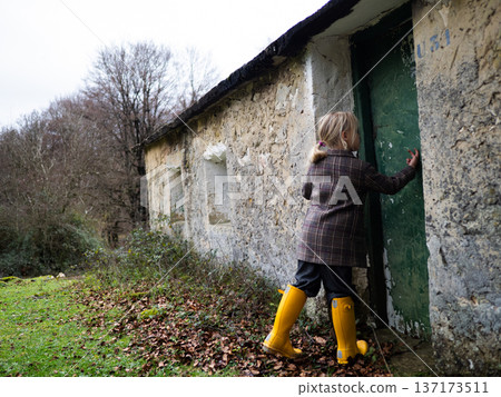 Child in yellow boots exploring rustic stone house in woods 137173511