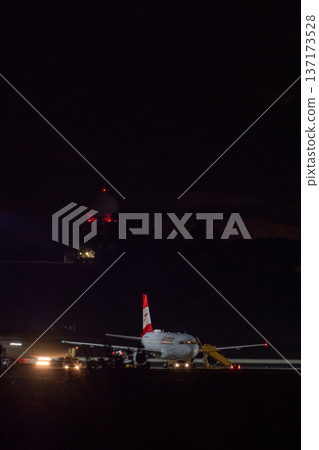 Passenger aircraft parked on airport tarmac with lights and control tower in background at night Passenger aircraft parked on airport tarmac with lights and control tower in background at night 137173528