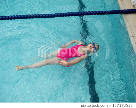 Girl in pink bathing suit floating on her back in clear water near blue lane divider Girl in pink bathing suit floating on her back in clear water near blue lane divider 137173553