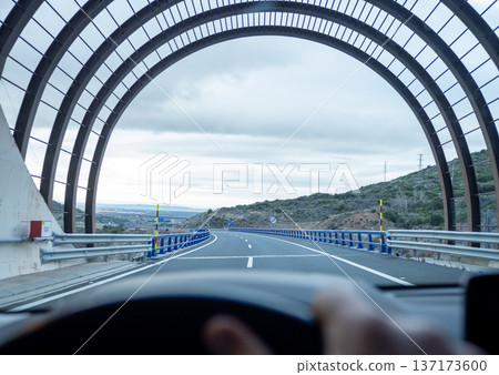 Wide perspective of a modern transportation tunnel with decorative metal ribs looking out onto a winding road and hills Wide perspective of a modern transportation tunnel with decorative metal ribs looking out onto a winding road and hills 137173600