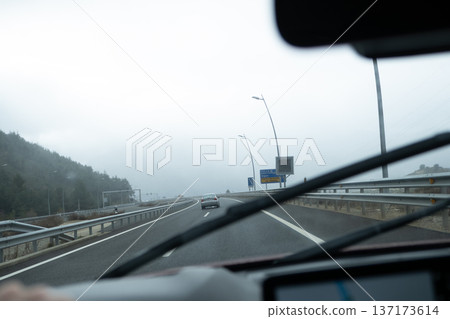 View through the windshield of a car moving along a misty motorway with traffic signs and low visibility 137173614