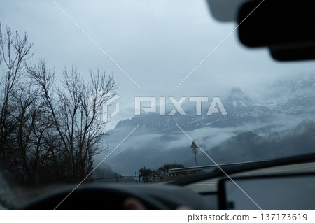 View from inside a vehicle of snow capped mountains partially hidden by low clouds and fog during a road trip View from inside a vehicle of snow capped mountains partially hidden by low clouds and fog during a road trip 137173619