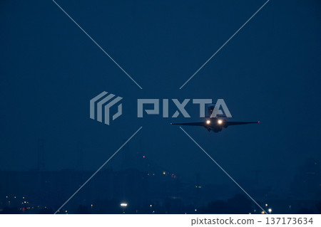 Commercial airliner ascending after departure from airport with bright landing lights against dark background Commercial airliner ascending after departure from airport with bright landing lights against dark background 137173634