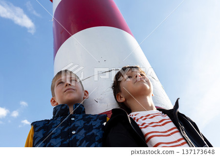 Two boys under lighthouse looking up, childhood dreams, future and direction, coastal lifestyle. Low angle Two boys under lighthouse looking up, childhood dreams, future and direction, coastal lifestyle. Low angle 137173648