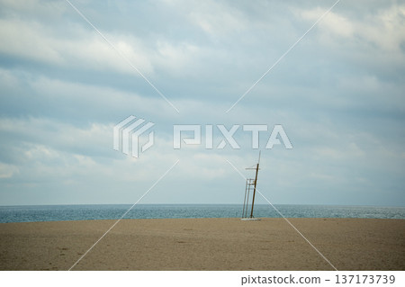 Minimalist view of a tall lifeguard chair standing on a sandy beach under a cloudy sky 137173739