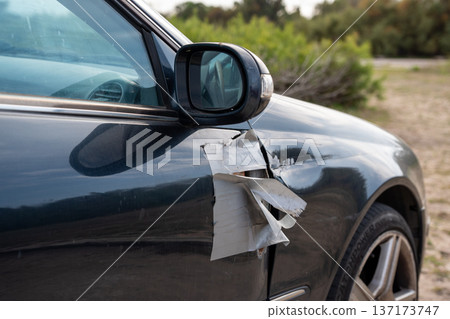 Side view of a dark car showing body damage held together by silver duct tape on the door 137173747
