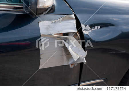 Close up of a dark vehicle body with a damaged panel held by adhesive tape 137173754