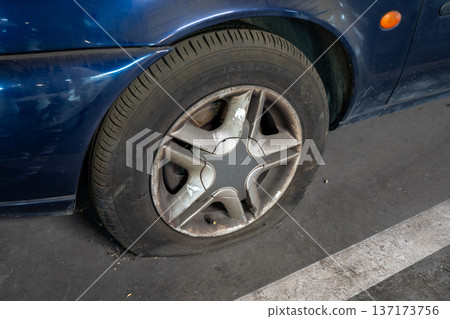 Detailed view of a deflated rubber tire and metal rim on an old blue vehicle 137173756