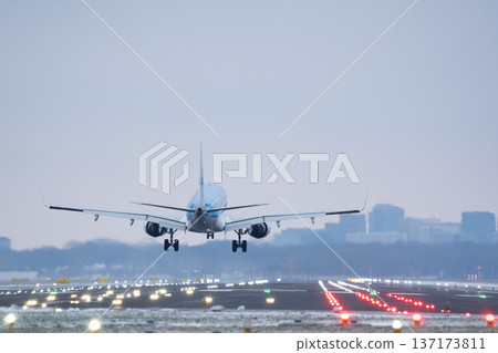 Commercial flight descending for landing on runway with city skyline in background 137173811