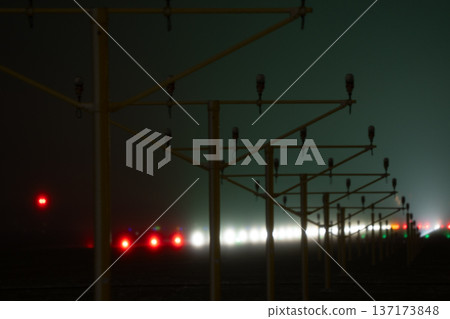 Yellow approach light structures standing in the mist at the edge of an airport runway during nighttime 137173848