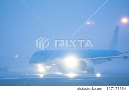 Side view of a blue commercial airplane taxiing on the airfield during cold foggy weather conditions at the airport Side view of a blue commercial airplane taxiing on the airfield during cold foggy weather conditions at the airport 137173864