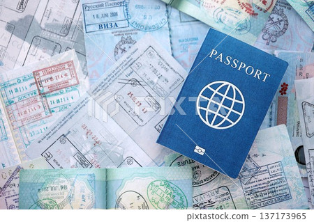One fictional passport on big amount of passport pages full of colorful stamps after travel and border crossing. Tourism and border control concept. Immigration and travel around the world One fictional passport on big amount of passport pages full of colorful stamps after travel and border crossing. Tourism and border control concept. Immigration and travel around the world 137173965
