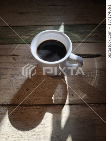 The shadow of a coffee cup falling on a wooden table - a moment of silence and rest The shadow of a coffee cup falling on a wooden table - a moment of silence and rest 137174061