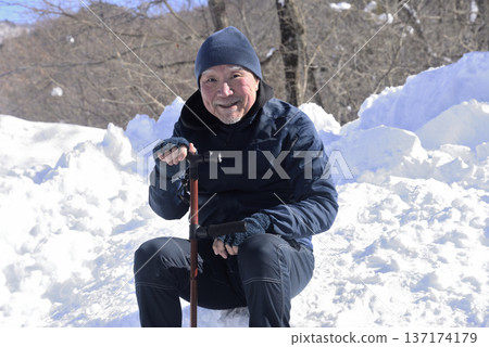 An elderly man taking a break from rehabilitation using a cane in a snowy country 137174179