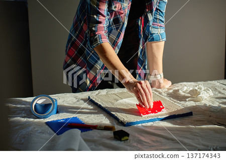Person pressing red plastic scraper into thick paste to create circular textured lines 137174343