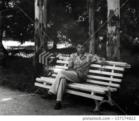 Vintage portrait of a handsome young man sitting on a park bench. Retro photo, 1959. Vintage portrait of a handsome young man sitting on a park bench. Retro photo, 1959. 137174822