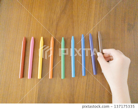 Child's hand arranging the ninth crayon on a wooden table Child's hand arranging the ninth crayon on a wooden table 137175335