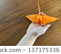 一個孩子手裡拿著一隻橘色的摺紙鶴 137175336