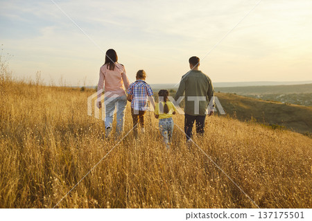 Parents and children walking in golden meadow at sunset, family togetherness Parents and children walking in golden meadow at sunset, family togetherness 137175501