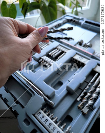 A woman's hand holds drills over an open toolbox 137175623