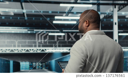 Technician walking in data center workplace with multiple rows of fully operational mainframes. Worker overseeing server farm built for storage enterprise solutions systems, camera B Technician walking in data center workplace with multiple rows of fully operational mainframes. Worker overseeing server farm built for storage enterprise solutions systems, camera B 137176561