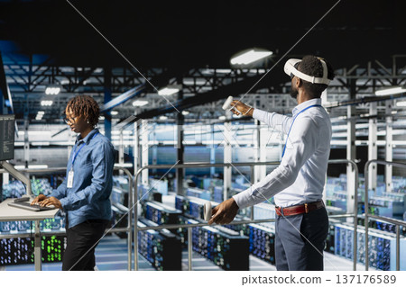 Data center programmer on industrial platform using virtual reality tech, collaborating on tasks. Server room IT professionals visualizing large language model architecture using VR headset. 137176589