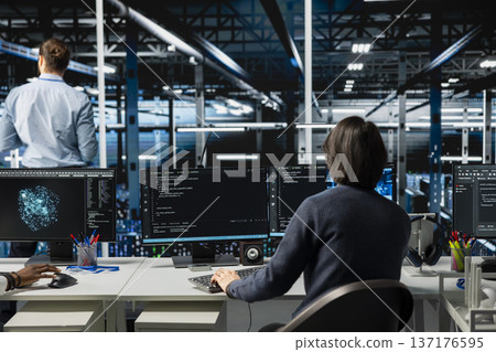 System administrator in server room using devices to review infrastructure diagnostics. IT expert in data center office analyzing performance data to maintain system uptime 137176595