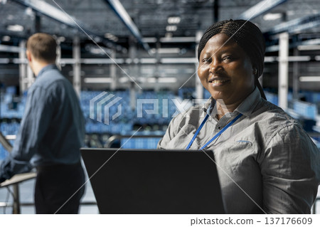 Close up of smiling worker in server farm next to colleague upgrading hardware for increased storage capacity. Jolly african american data center admin and coworker doing maintenance 137176609