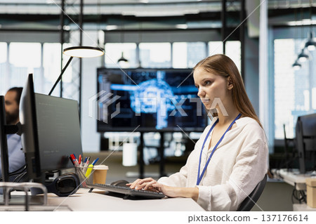 Junior dev in tech startup utilizing AI to optimize performance and forecast issues. Young female engineer writing code in office, training machine learning models using PC 137176614